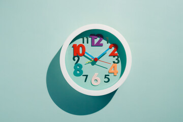 Photos of round children's wall clocks with multi-colored numbers on blue background with shade. Top View. Cheerful watch with multi-colored dial. flat lay