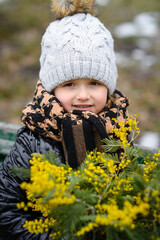 little girl holds a bouquet of mimosa in the park in early spring and smiles