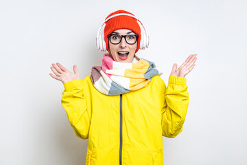 Cheerful surprised young girl in headphones, in a yellow jacket on a light background.