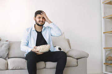 Brunette guy sitting on a coach and watching football at home