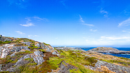 An island, islets and a lighthouse off in the distance. Clear skies, summer day