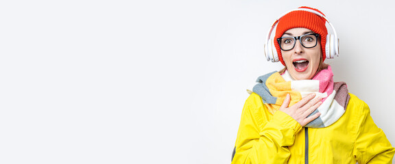 Cheerful surprised young girl in headphones, in a yellow jacket on a light background. Banner.