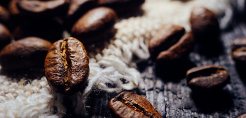 Macrophotography of coffee beans lie on textured wood and burlap. Fresh harvest aromatic coffee. Selective focusing. Back for cafe, restaurant or coffee shop. advertising banner