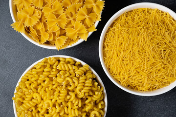 Close up of several types of dry pasta in a plate on dark background