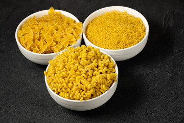 Close up of several types of dry pasta in a plate on dark background