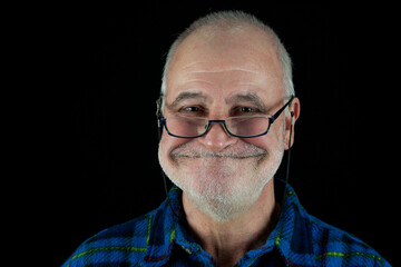 Old man with glasses grins mischievously at the camera against a black background.