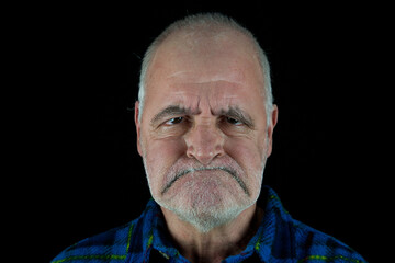 An old man looks angrily at the camera with his mouth pulled down.
