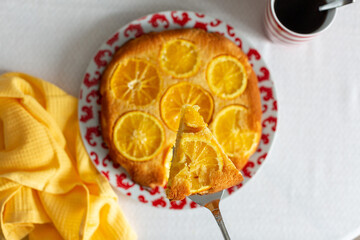 A juicy piece of orange pie on the shoulder blades to lift above the table, on the table a mug of tea and a yellow towel