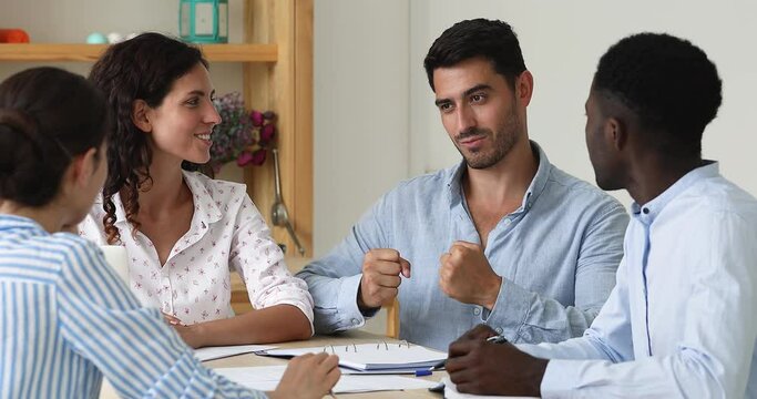Confident team leader makes speech at morning briefing. Four multi ethnic office employee staff members take part in group meeting, listen ideas of colleague gather in boardroom. Seminar event concept