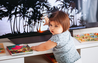 Side view of a little cute girl watching television with toys. The toddler girl watch tv.