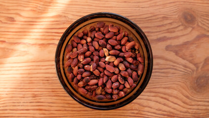 Small bowl of roasted peanuts on wooden table background. Copy space text.