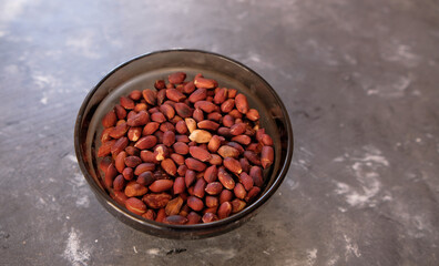 Small bowl of roasted peanuts on a gray table background.
