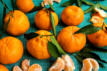 frische saftige clementinen mit blättern und fruchtscheiben vor türkisfarbenen hintergrund
