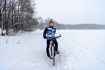 Fototapeta na wymiar Russian bicyclist on winter lake with forest on background, Moscow Region