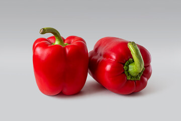 Two ripe bright red bell peppers on a light background