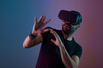 Young man in VR glasses excited interact with virtual reality in color neon light, future technology, education video gaming