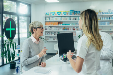 Obraz premium Two pharmacist giving prescription medications to senior female customer in a pharmacy