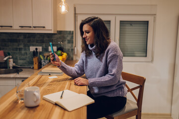 Hispanic woman is using smartphone for a video call while at home