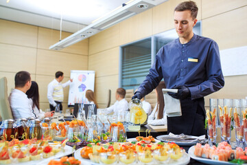 A young waiter pours drinks for catering.