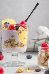 Vegan natural dessert. Granola with raspberries, blueberries and golden kiwi. Glass of muesli, berries and yogurt parfait on the table. Sweet and healthy breakfast. Selective focus. Vertical position.