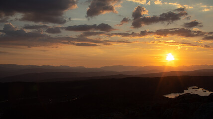 Sunset over Norwegian mountains, with scattered clouds, and a lake in the foreground