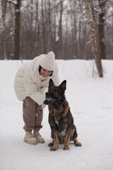 a girl in white hugs a dog against the background of snow and forest