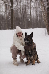 a girl in white hugs a dog against the background of snow and forest