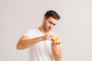 Portrait of dissatisfied young man with disgust picking bud of bad burger on white isolated...