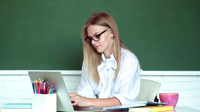Student preparing for test or exam. Young female student in glasses studying in shcool over blackboard background in the classroom.