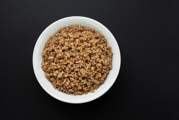 Bowl of buckwheat flakes on black background