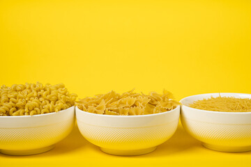 Close up of several types of dry pasta in a plate on yellow background