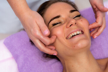 Naklejka premium Relaxing massage. European woman getting facial massage in spa salon, side view