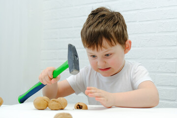 a boy of 4-5 years old sits at a table, breaks walnuts with a hammer. Funny facial expression,...