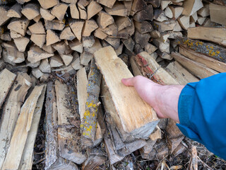 a man's hand holds a log pulled from a pile of firewood