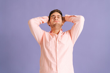 Portrait of sad young man holding head and thinking about problem solution on pink isolated background in studio. Annoyed male reflecting on mistake he made and feeling disappointed.