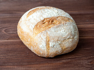 Close-up of a round loaf of wheat bread lying on a brown wooden background. Baking, bakery concept. Side view