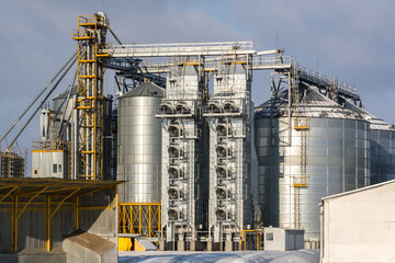 Obraz premium agro silos granary elevator in winter day in snowy field. Silos on agro-processing manufacturing plant for processing drying cleaning and storage of agricultural products, flour, cereals and grain.