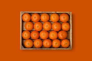 Wooden crate of ripe tangerines on an orange background. Clementine mandarins in a wooden box. View...