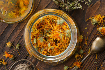 Glass jar of dried calendula flowers, cup of healthy calendula herbal tea, thyme medicinal herbs on...