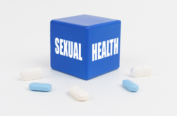 On a white surface are pills and a blue cube that says - SEXUAL HEALTH