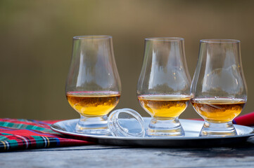 Tasting glasses of scotch whisky strong drink and red Scottisch tartan on old outdoor table