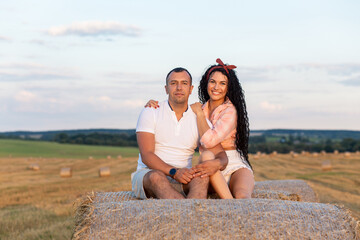Loving couple in a field on rolls of straw.