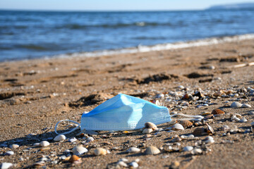 A disposable blue face mask on the beach sand. Waste in nature.