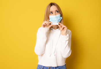 Young woman wearing surgical mask showing a test isolated over yellow background. © Danko