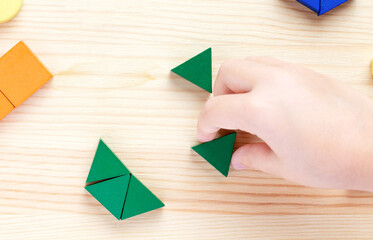 A child plays with colored blocks constructs a model on a light wooden background - 482241308