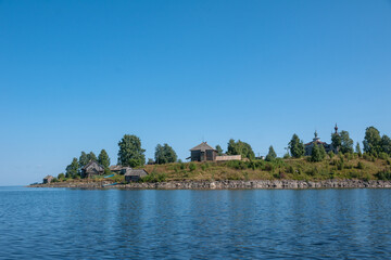 Fototapeta premium View of Church of Nativity of Virgin and old wooden sheds on shore of Lake Segozero in summer, Karelia, Russia