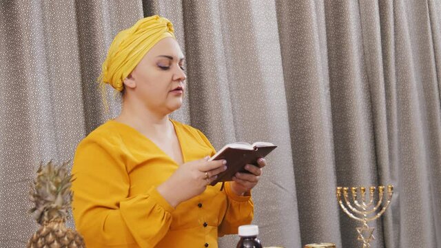 A Jewish woman in a traditional headdress reads a Shabbat meeting prayer