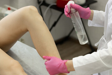 depilation of the girl's legs, the hands of the master in pink gloves treat the skin with disinfection