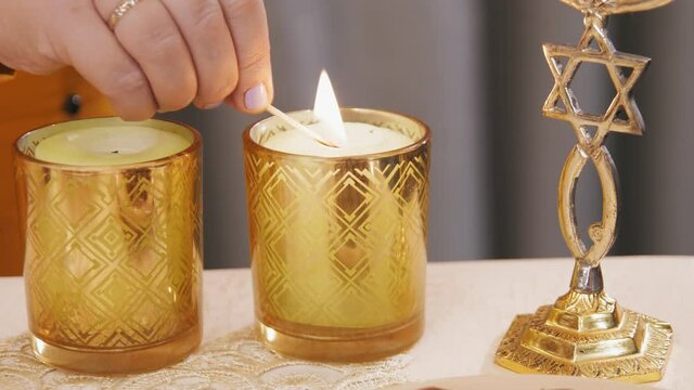 hand Jewish woman lights Shabbat candles on the table.