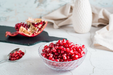 Grains of a ripe pomegranate in a bowl and in a spoon and a part of a pomegranate on a light table. Organic natural food. Lifestyle
